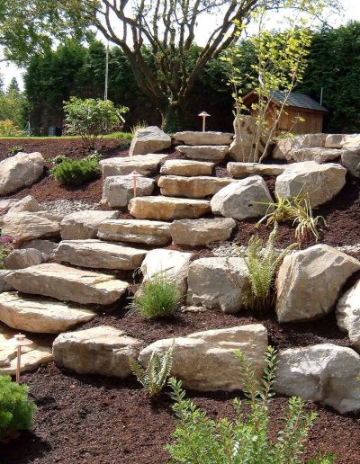 A Greenhaven Landscapes-designed Vancouver WA backyard rock staircase and stone retainer wall with new bark and shrubbery