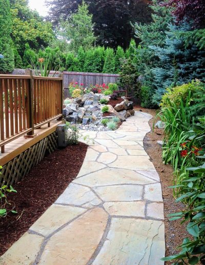 A Greenhaven Landscapes design customer's Vancouver WA backyard stone walkway path with wood deck and stone waterfall water feature