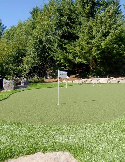 A Greenhaven Landscapes-designed Vancouver WA synthetic turf putting green with large rock landscaping surrounding it