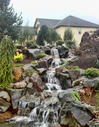 A Greenhaven Landscapes-designed Vancouver WA water feature - a backyard stone waterfall and stone retaining wall landscape design