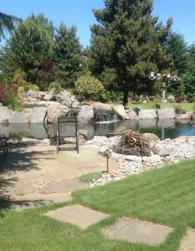 A Greenhaven Landscapes design customer's Vancouver WA large pond with stone walls and waterfall water feature next to stone patio and walkway