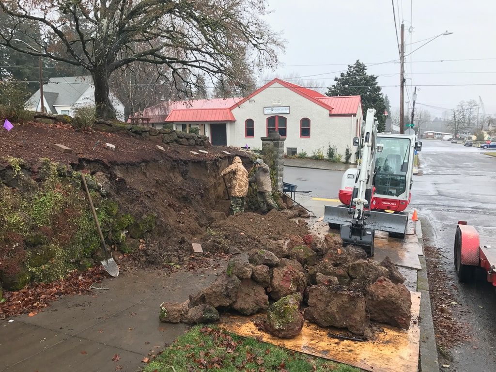 Greenhaven Landscapes team remove a stone retaining wall with machinery and shovels in Vancouver WA