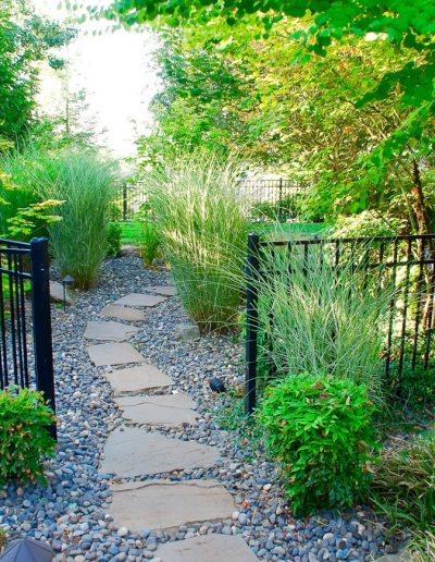A Greenhaven Landscapes design customer's Vancouver WA back yard with a gate, stone walkway, and beautiful plants, trees lining the path