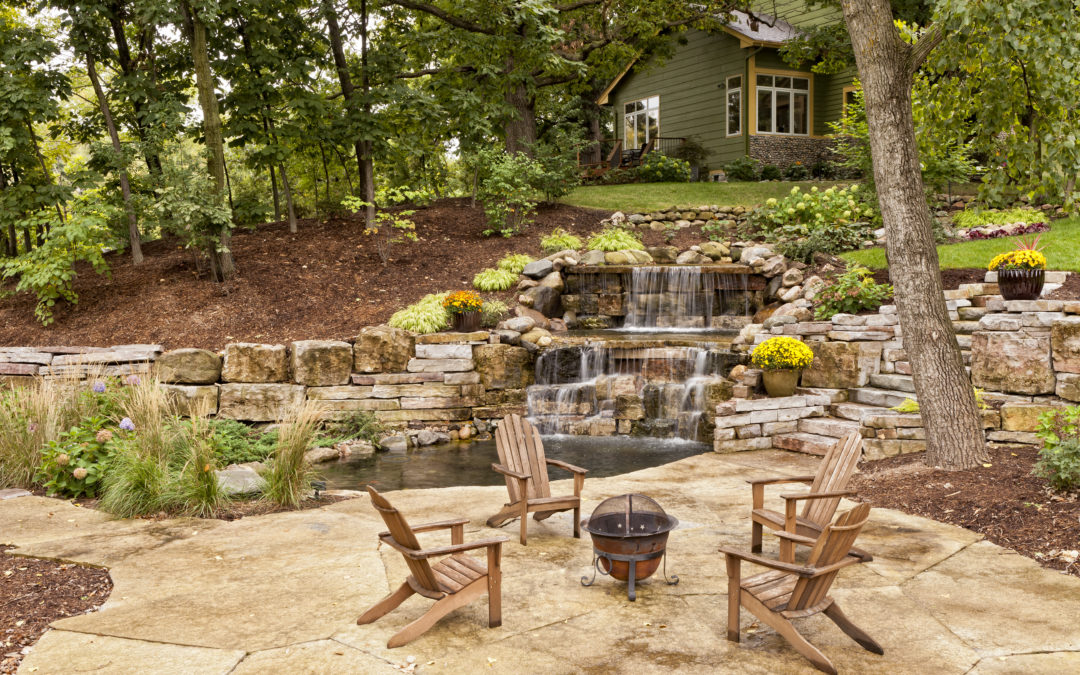 Beautiful landscaping with waterfall, koi pond, and stone patio with wooded surroundings.