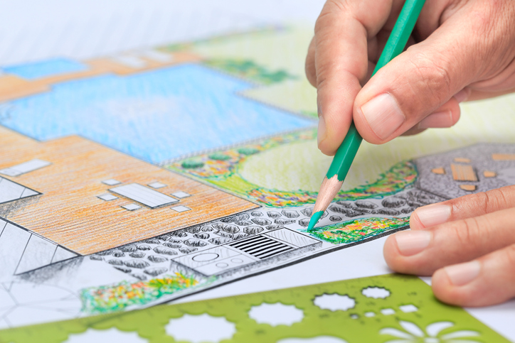 Image of a hand holding a green pencil adding detail to a landscape design drawing.
