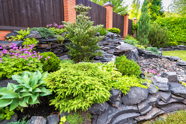 Image of a terraced landscape design with new fence, stones, plants, flowers, and water feature.