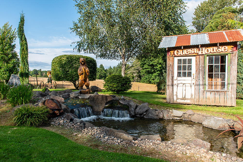 a wood carving of a bear holding a fish overlooks a waterfall from Greenhaven Landscapes