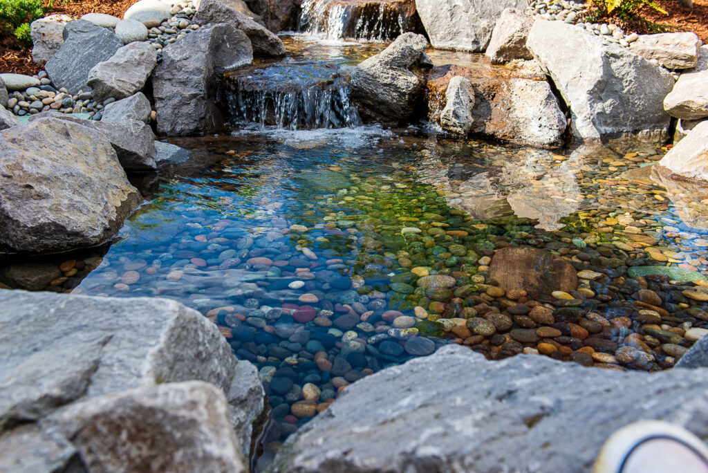 waterfall flows into a small clear pond with pebbles under the surface