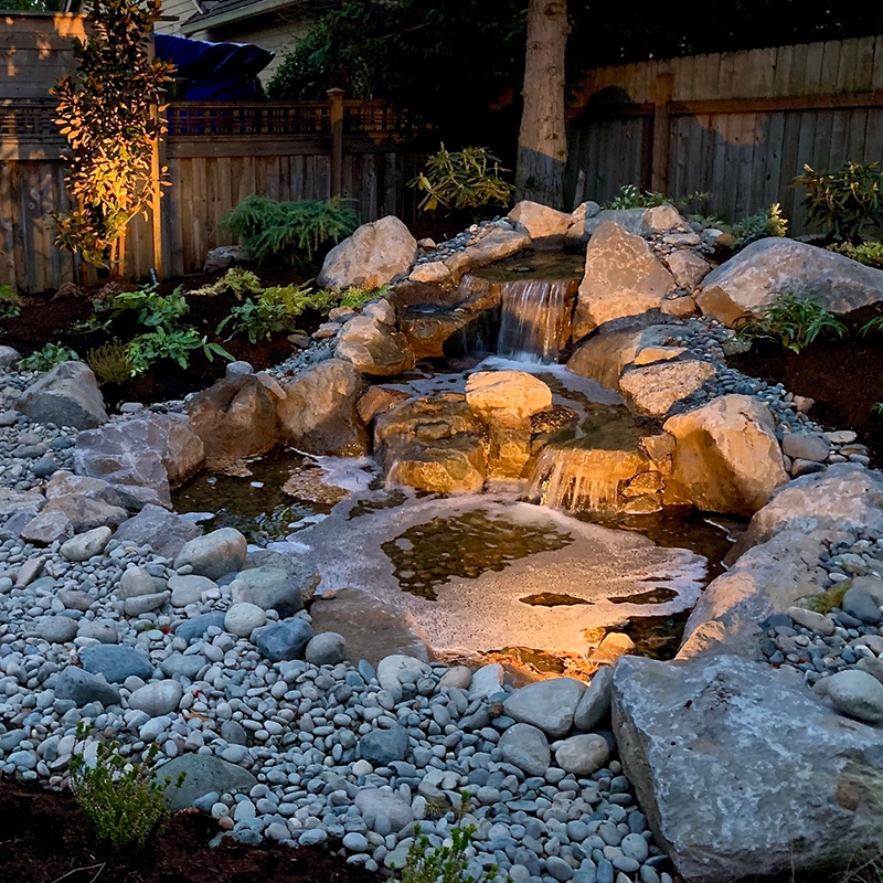 a water feature glowing at night by Greenhaven Outdoor Living